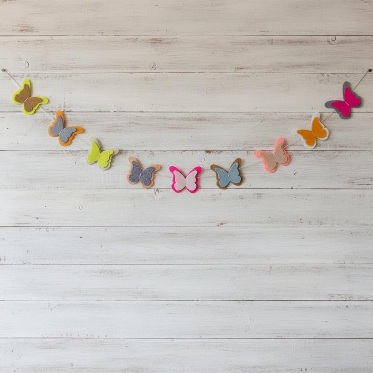 Handmade colourful felt butterfly garland against a white wooden backdrop