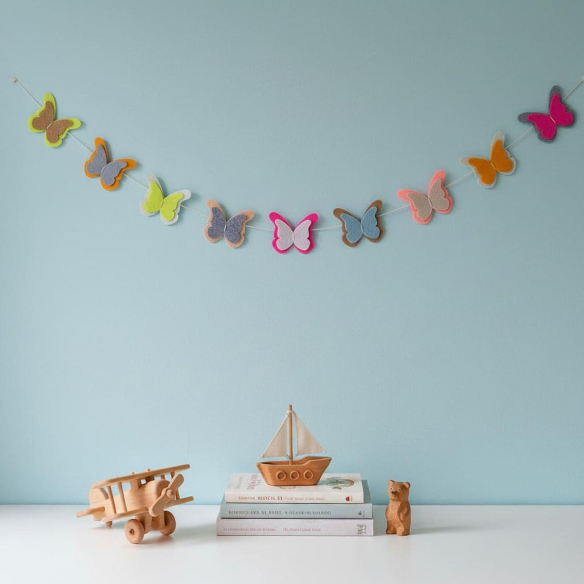 Colourful felt butterfly garland styled above wooden toys against a light blue wall